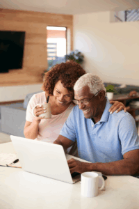 Smiling couple sitting at a kitchen counter, looking at a laptop together — representing peace of mind through organized digital legacy planning.