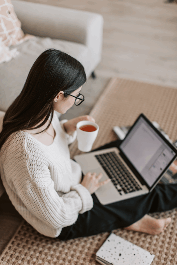 Person sitting comfortably on floor with laptop and tea, reviewing content in a relaxed digital workspace.