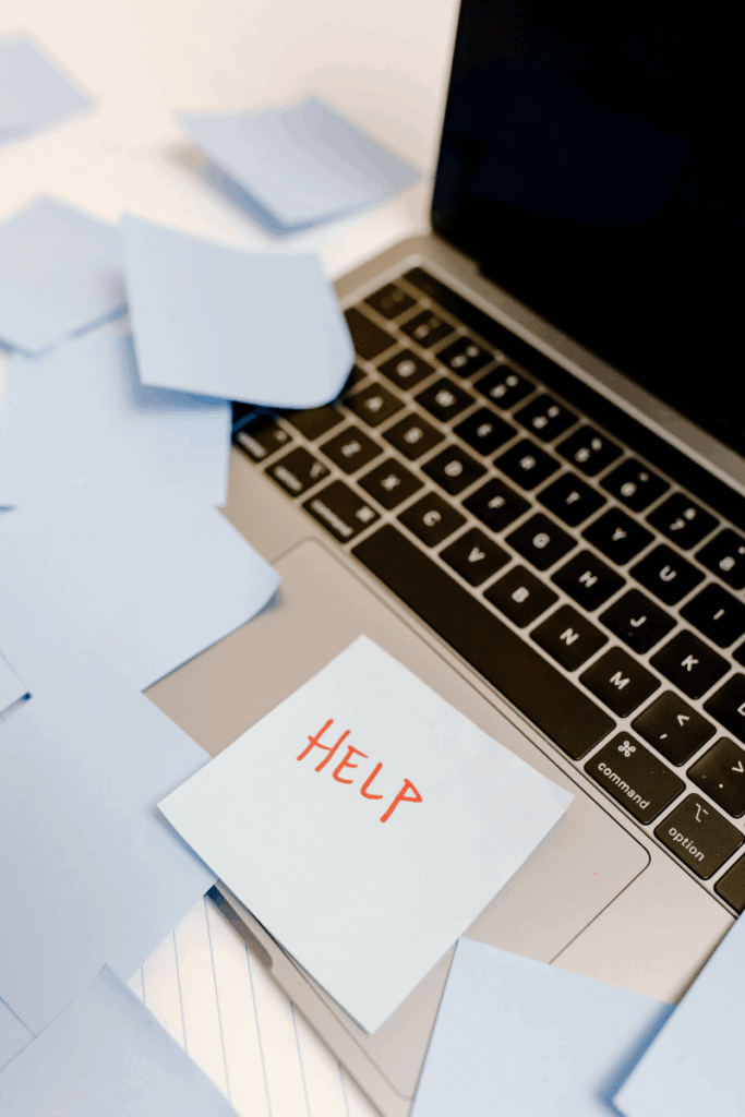 Laptop covered in sticky notes with one reading “HELP,” representing digital overwhelm and scattered tasks in small business operations.